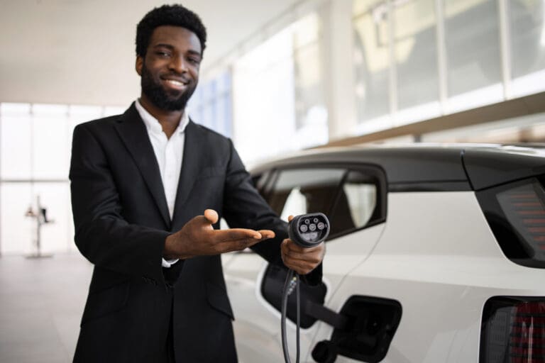 Confident car dealer in suit showcasing electric SUV at modern dealership. Representing eco-friendly, sustainable transportation. EV charger in hand indicates focus on electric mobility.